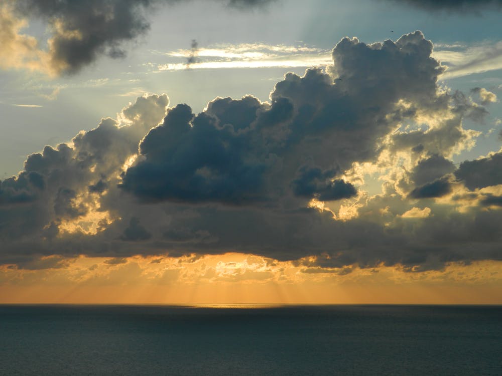 бесплатная Солнце за белыми облаками над водоемом в дневное время Стоковое фото