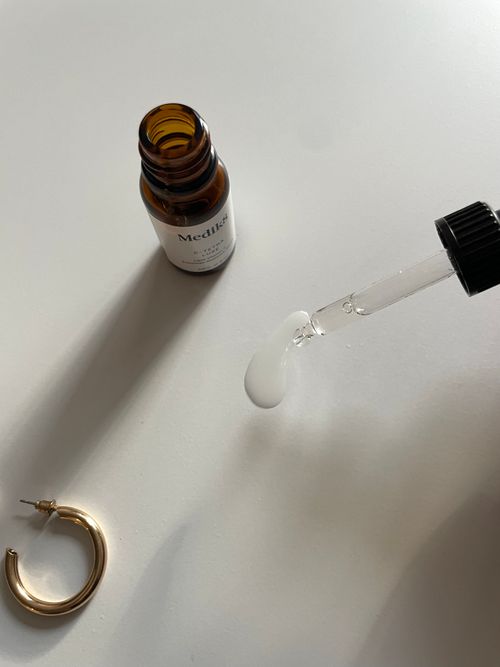 Free Close-up shot of a dropper with serum beside an open cosmetic bottle and a golden earring on a white surface. Stock Photo