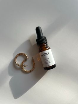 Elegant minimalist composition featuring serum bottle and jewelry with soft shadows on a plain background.