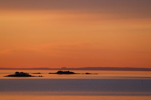 Free Serene sunset view over the waters of Cove Island Park, capturing vibrant orange hues and distant islands. Stock Photo