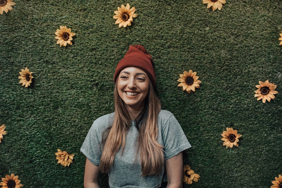 Cheerful woman in beanie smiling with sunflower backdrop.