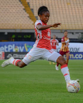 Dynamic action shot of a female soccer player kicking the ball in a stadium.