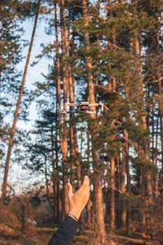 A close-up of a flying drone over a forest with a hand reaching out, captured outdoors.