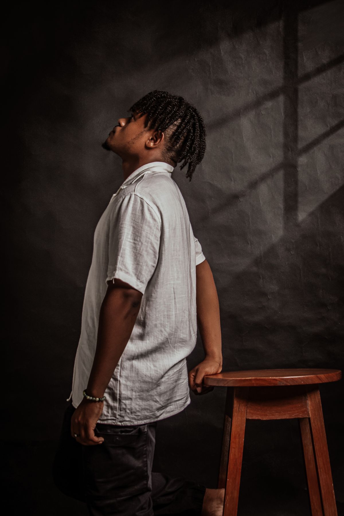 Retrato editorial em estúdio de homem usando camisa branca apoiado em banqueta de madeira