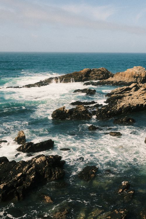 Free A stunning view of waves crashing against a rocky coastline under a clear blue sky. Stock Photo