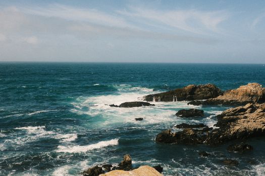 Dynamic seascape with waves crashing against rugged rocks under a clear sky. Perfect for travel and nature themes.