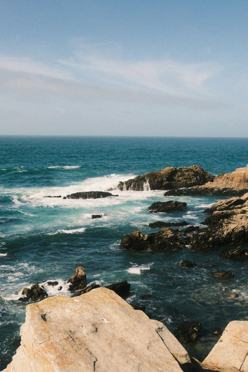 Free Beautiful rocky coast with waves crashing under a clear blue sky. Stock Photo