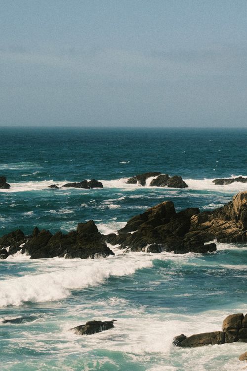 Free Powerful ocean waves crashing against rugged rocks under a bright sky, showcasing nature's raw beauty. Stock Photo