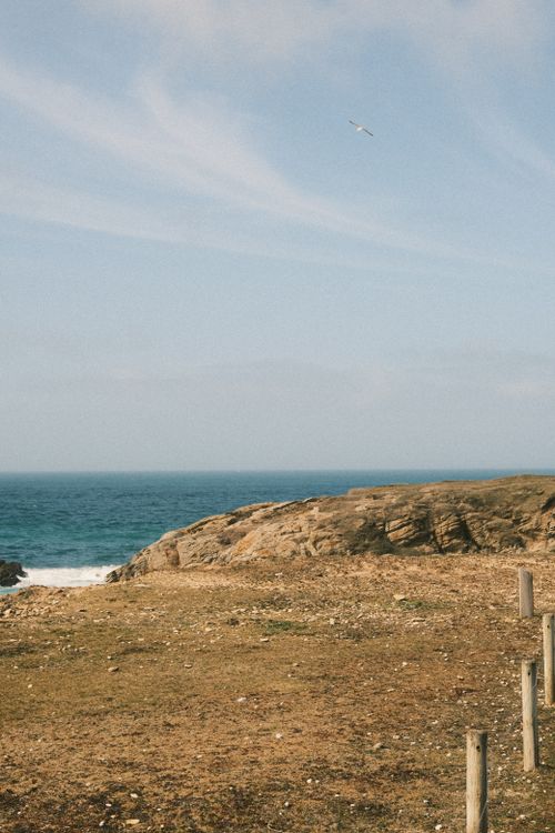 Free A serene coastal landscape featuring rocky shores and a flying bird against a blue sky. Stock Photo