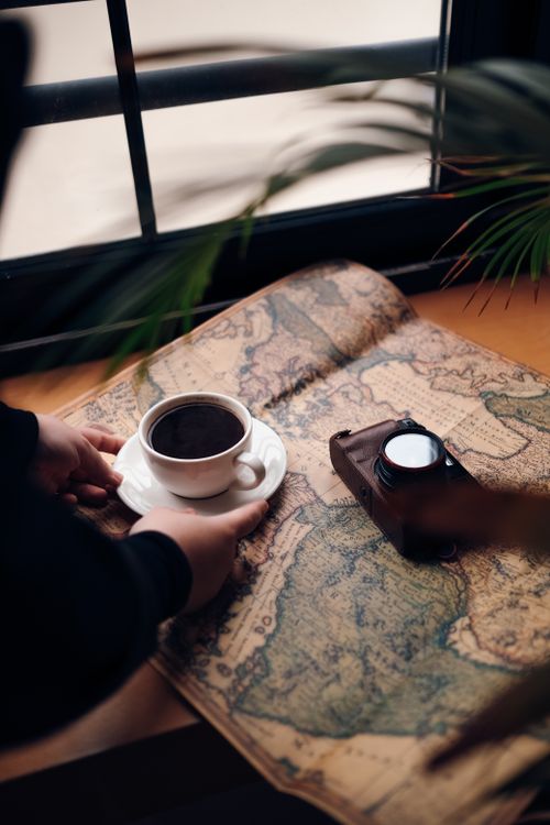 Free A cozy scene featuring a cup of coffee on a vintage map with a retro camera, evoking a sense of exploration. Stock Photo