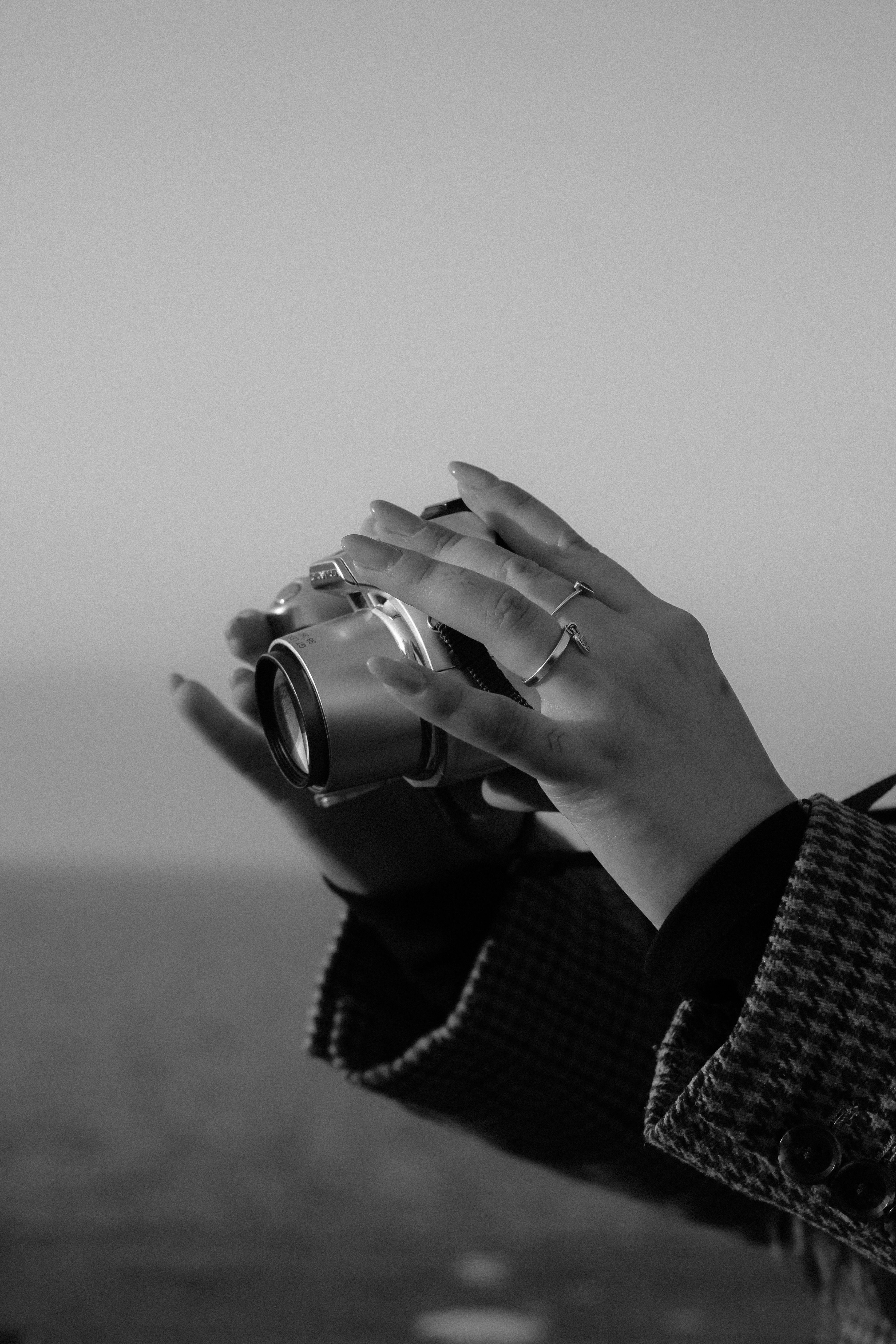 Close-up black and white shot of hands holding a camera, capturing a serene outdoor scene.