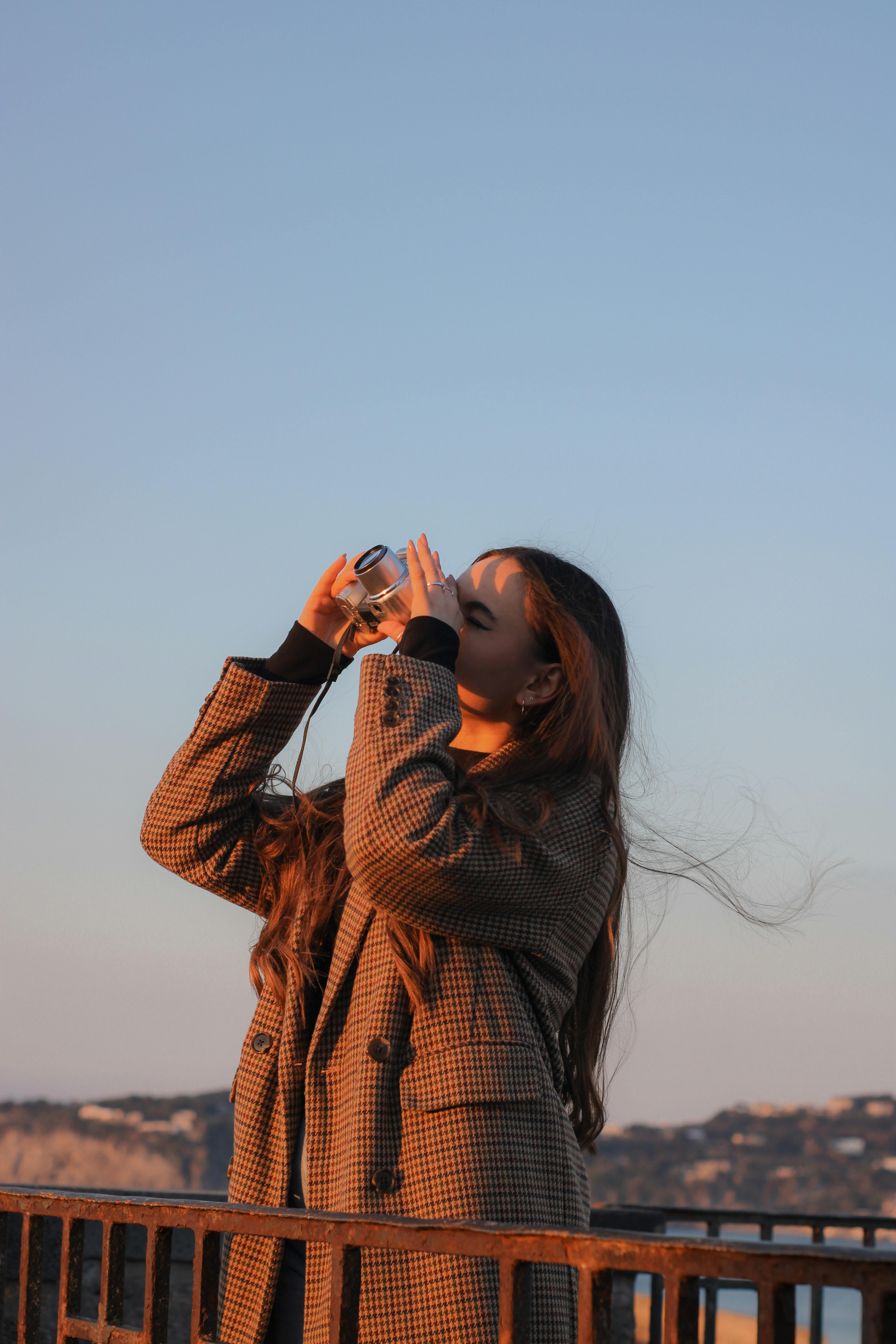 Woman using a camera to capture scenic views outdoors under a clear sky.