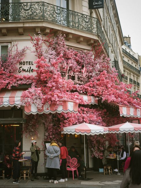 Cozy Parisian cafe adorned with vibrant pink flowers on a bustling city street.