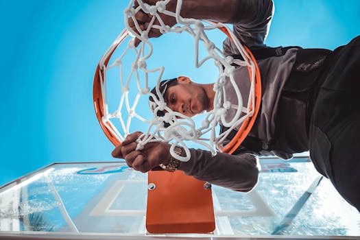 Close-up of a man adjusting a basketball hoop against a clear blue sky background.