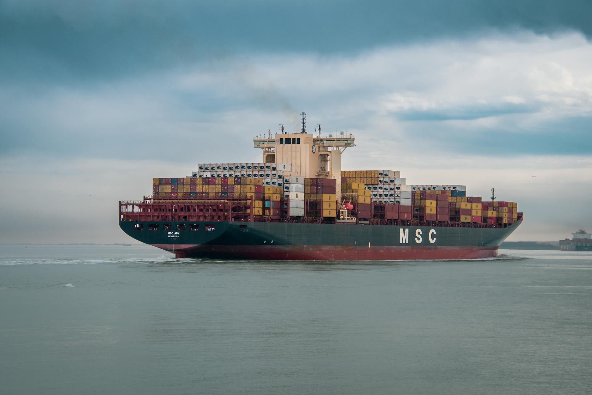 Massive cargo ship sailing on the ocean, carrying colorful containers under a cloudy sky.