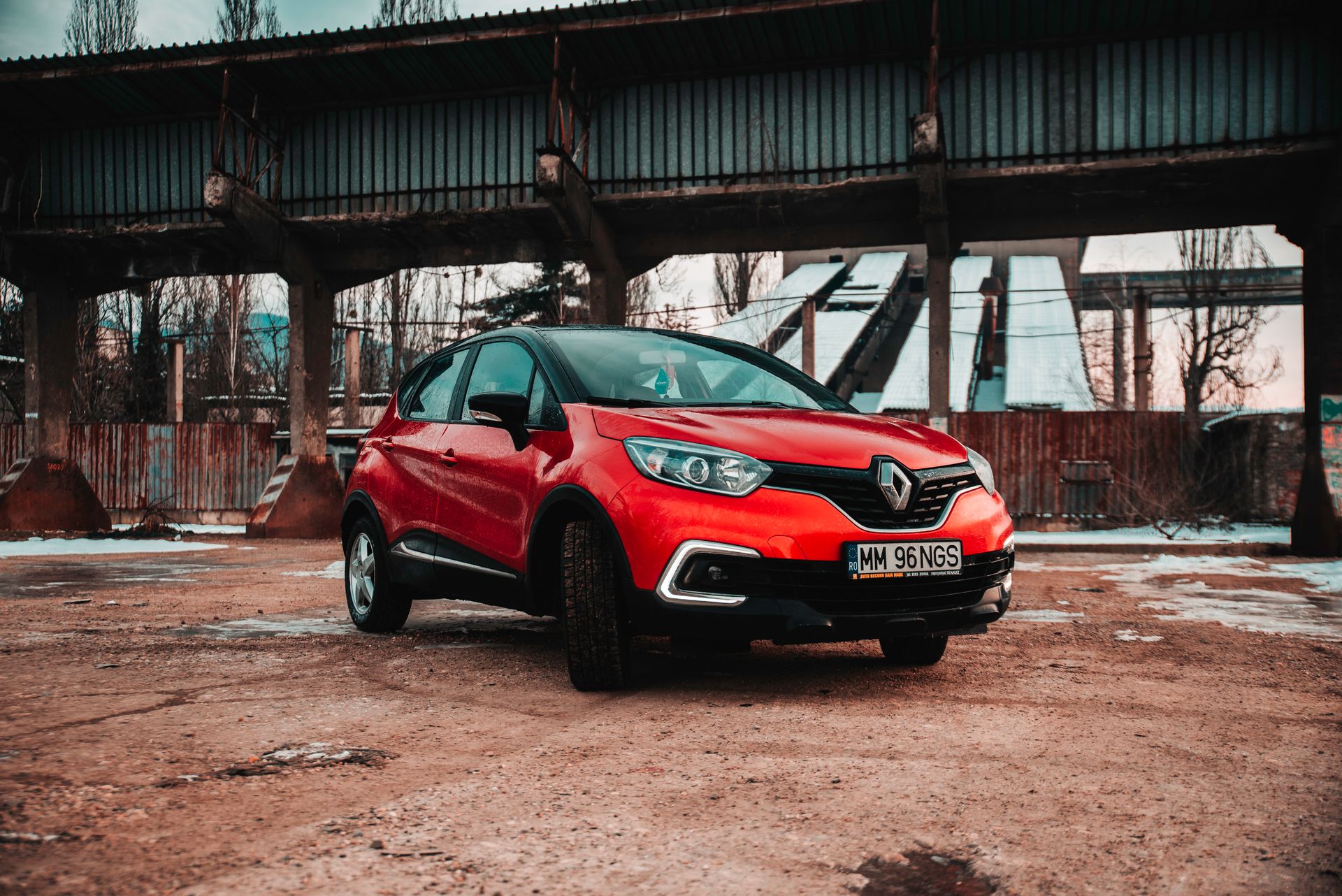 Striking red Renault Captur parked in a rugged industrial setting under a bridge.