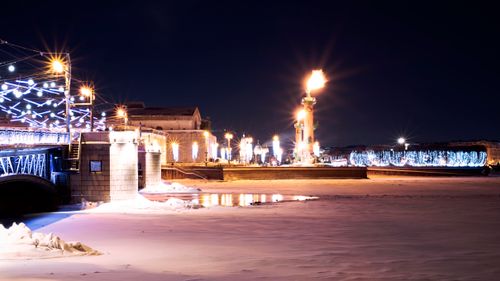 Free A vibrant night shot of a city with illuminated bridge and river covered in snow. Stock Photo