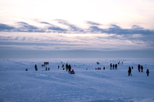 A serene winter scene with people enjoying a day in the vast snowy plains under a cloudy sky.