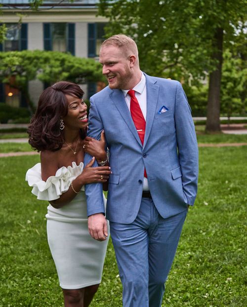 Free A happy couple in formal attire walking and embracing in a vibrant park setting. Stock Photo
