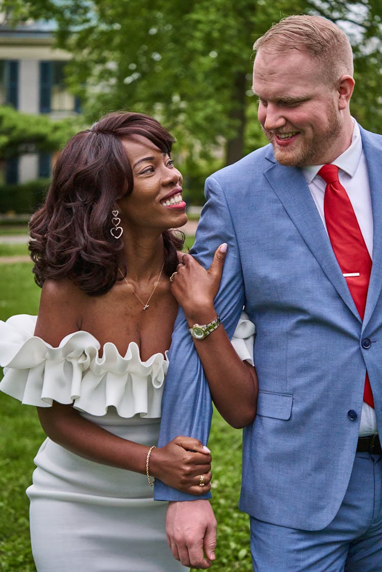 Bride And Groom Walking In A Park, Looking At Each Other And Smiling 