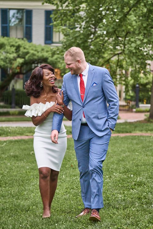 Free Happy interracial couple in elegant attire walking and smiling in a park setting. Stock Photo