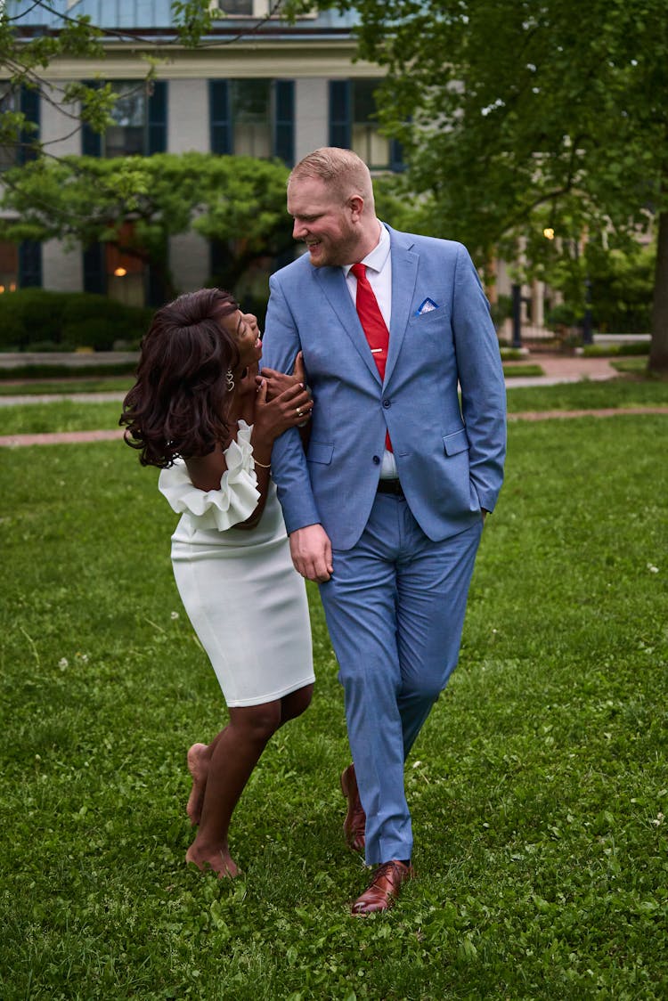 Bride And Groom Walking In A Park, Looking At Each Other And Smiling 