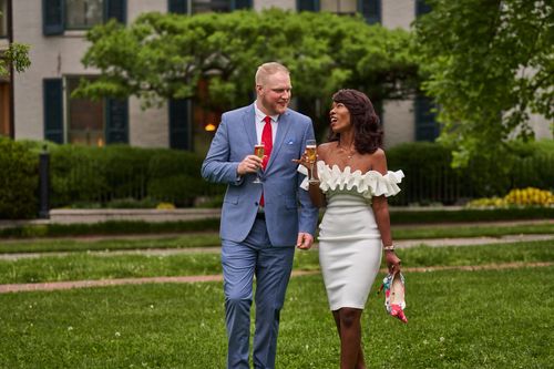 Free A well-dressed couple enjoys drinks in a scenic garden setting, exuding elegance and joy. Stock Photo