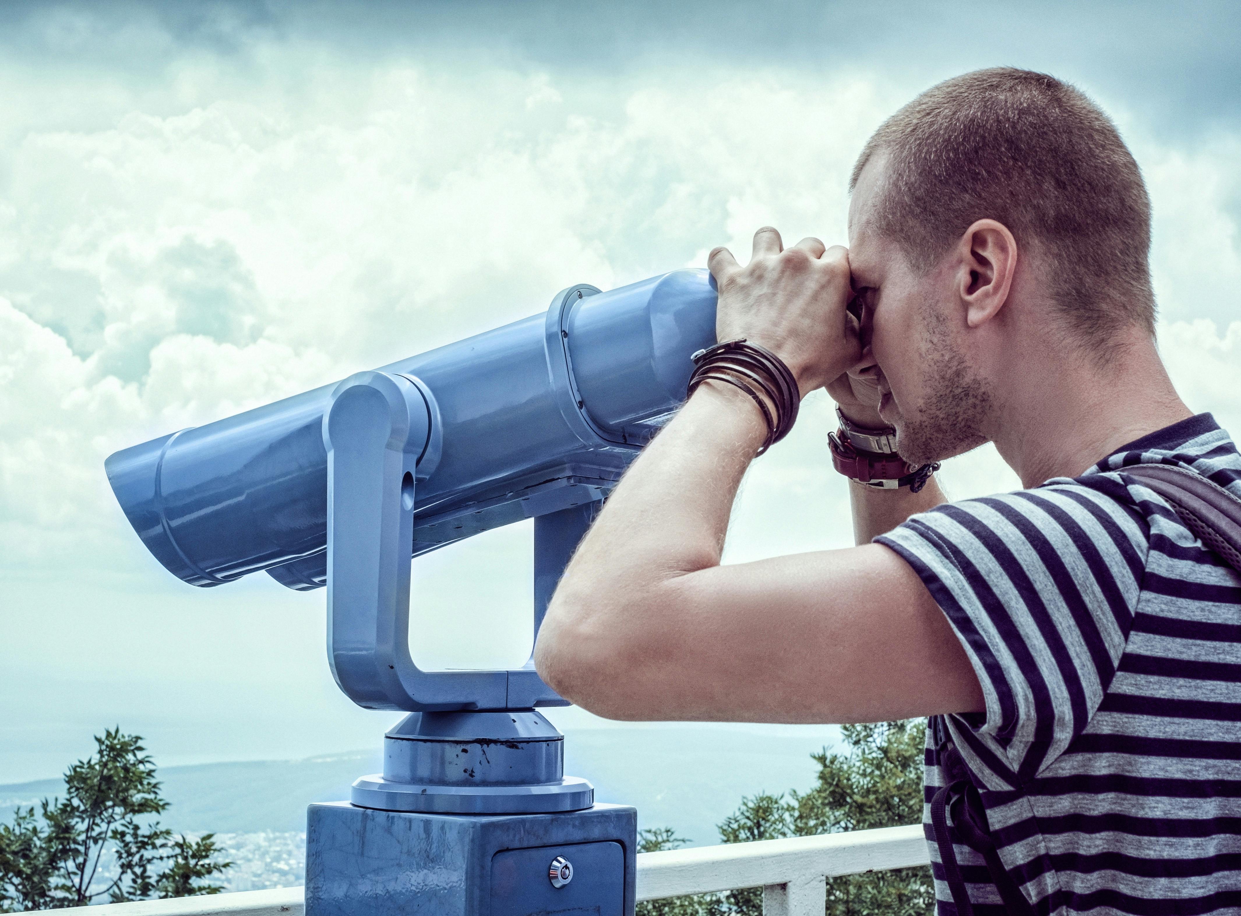 Person in White and Gray Stripes Crew Neck T Shit Using Telescope Near White Metal Handrails Under White Clouds during Daytime