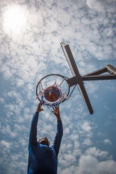 A man reaching for a basketball hoop on a bright day, showcasing energy and motion.