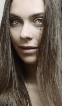 Close-up portrait capturing a young woman with brown hair and green eyes, smiling gently in a studio setting.
