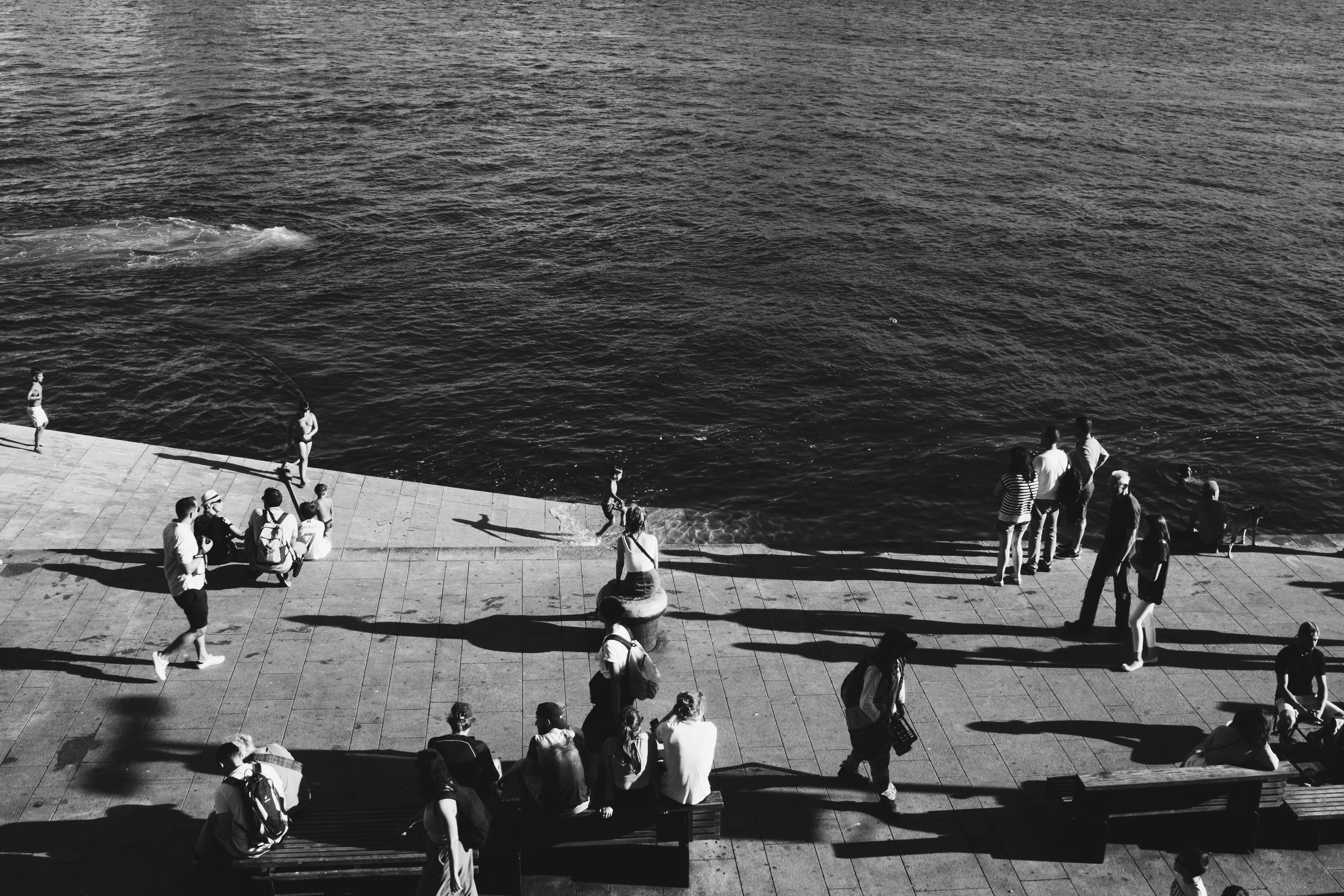 单色图像捕捉到人们在阳光明媚的海滨享受时光，投下长长的阴影