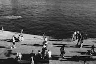 单色图像捕捉到人们在阳光明媚的海滨享受时光，投下长长的阴影