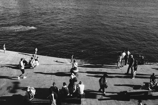 单色图像捕捉到人们在阳光明媚的海滨享受时光，投下长长的阴影