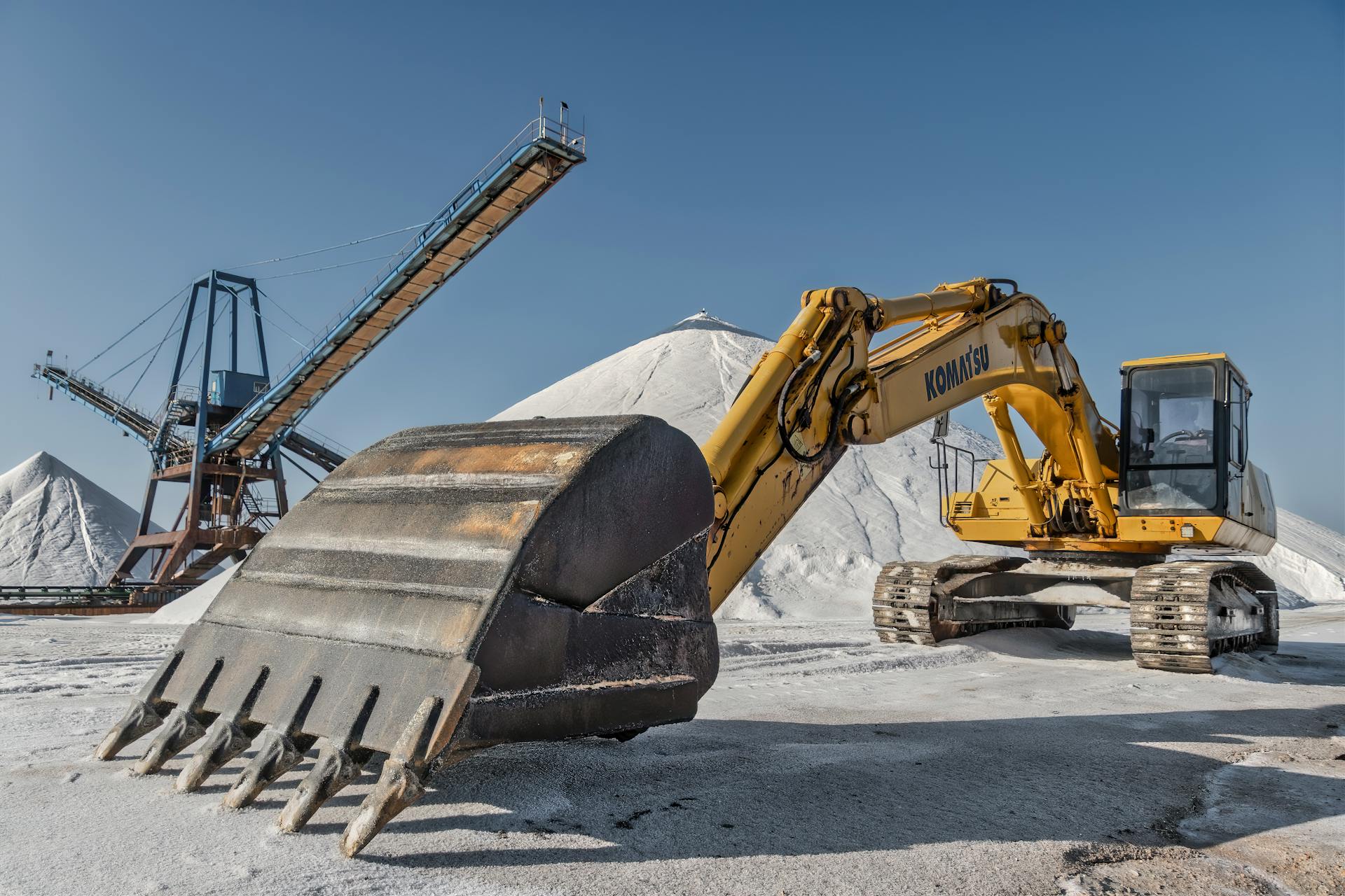 Excavator and conveyor system in a snowy quarry under clear skies.
