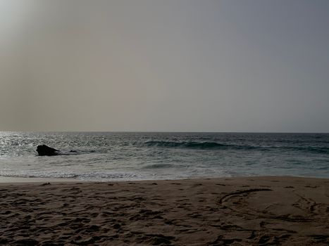 Tranquil beach scene in Lisbon, Portugal, with gentle waves and setting sun.