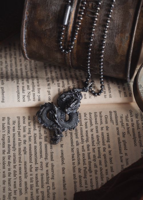 Free A detailed metal Chinese dragon necklace resting on an open book, symbolizing fantasy and culture. Stock Photo