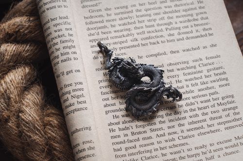 Free Intricate dragon pendant resting on an open book page with a rustic rope in view. Stock Photo