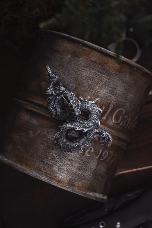 Free A silver dragon pendant on a rustic metal cup, creating a vintage and artistic look. Stock Photo