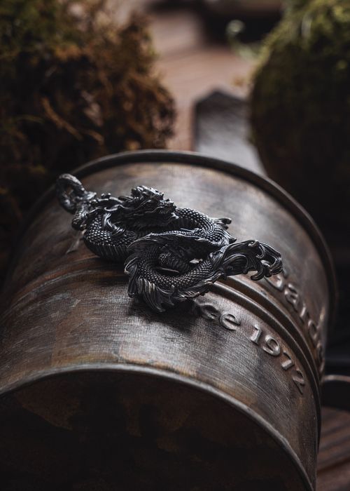 Free A detailed dragon keychain rests on a rustic metal cup, creating a moody, vintage scene. Stock Photo