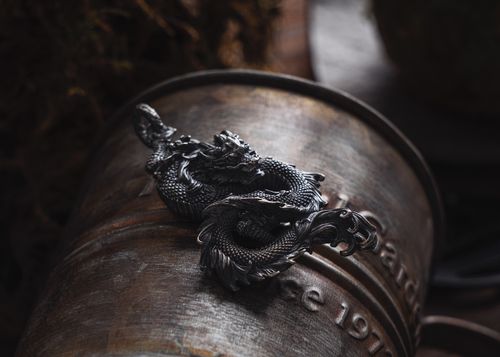 Free Detailed dragon metal pendant placed on a rustic, textured metal barrel, offering a retro still life scene. Stock Photo