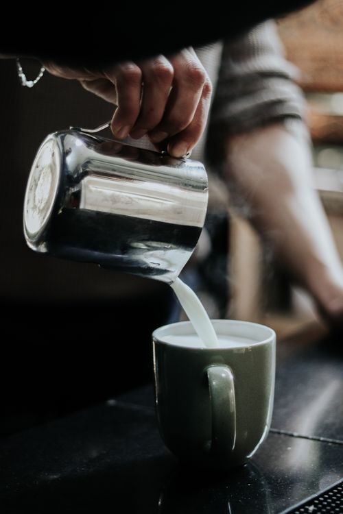 Free A person pours steaming milk into a cappuccino mug, creating a warm beverage. Stock Photo