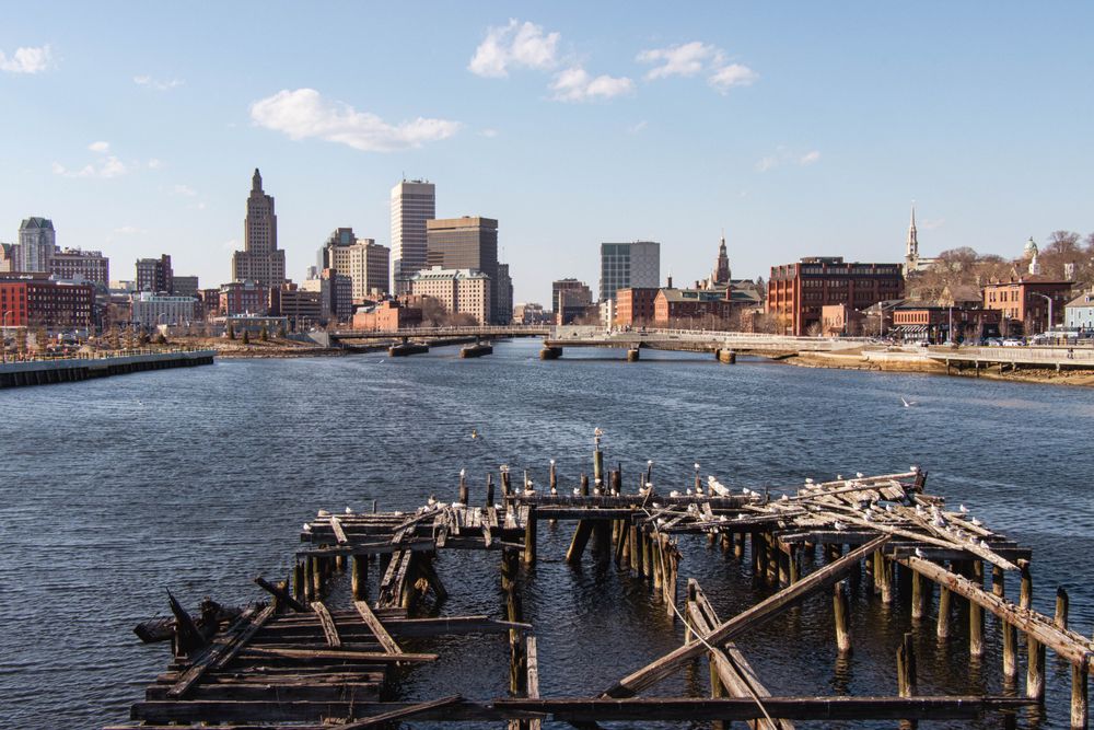 Explore the city skyline and river with a foreground of an old wooden dock during a bright day.