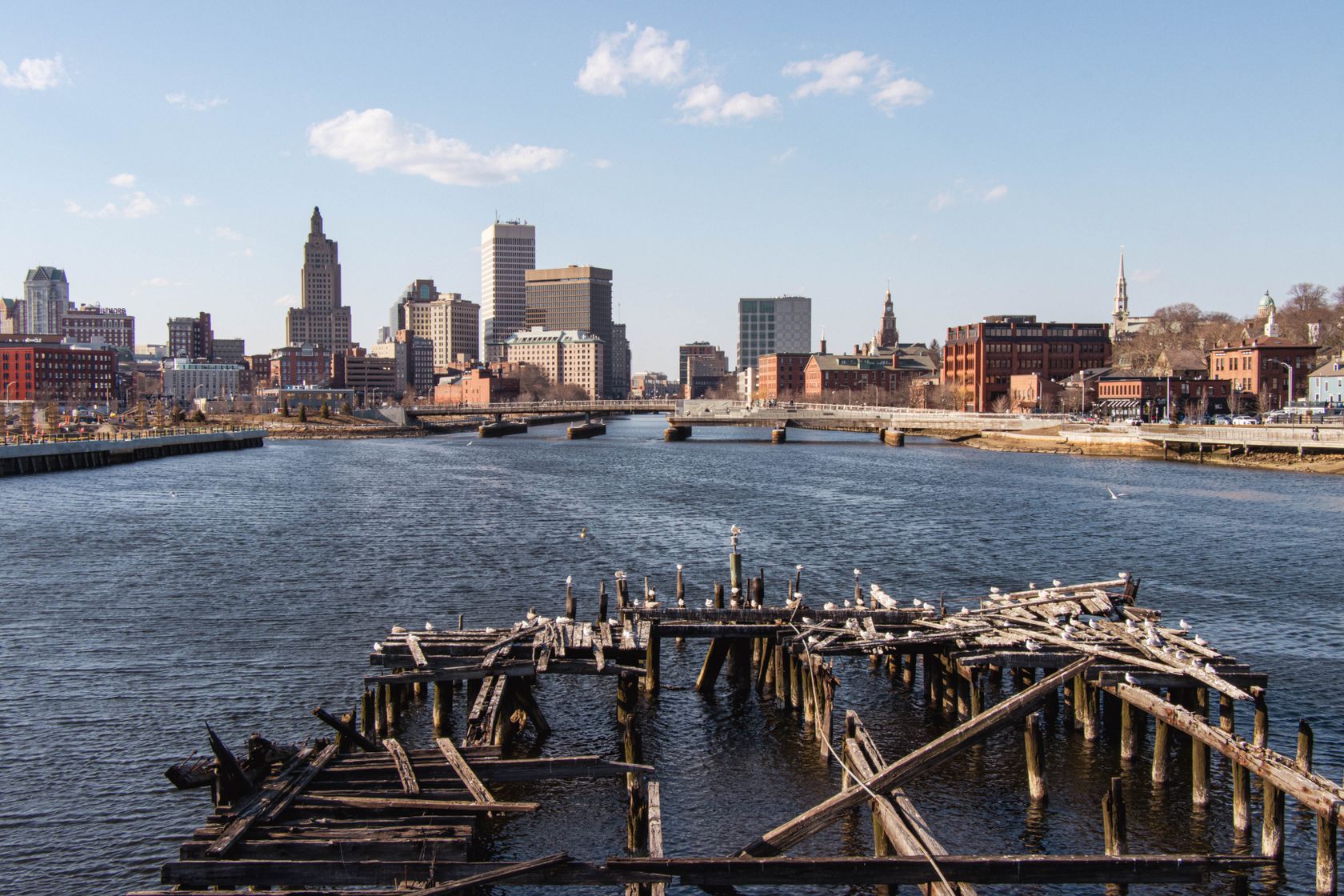 Explore the city skyline and river with a foreground of an old wooden dock during a bright day.