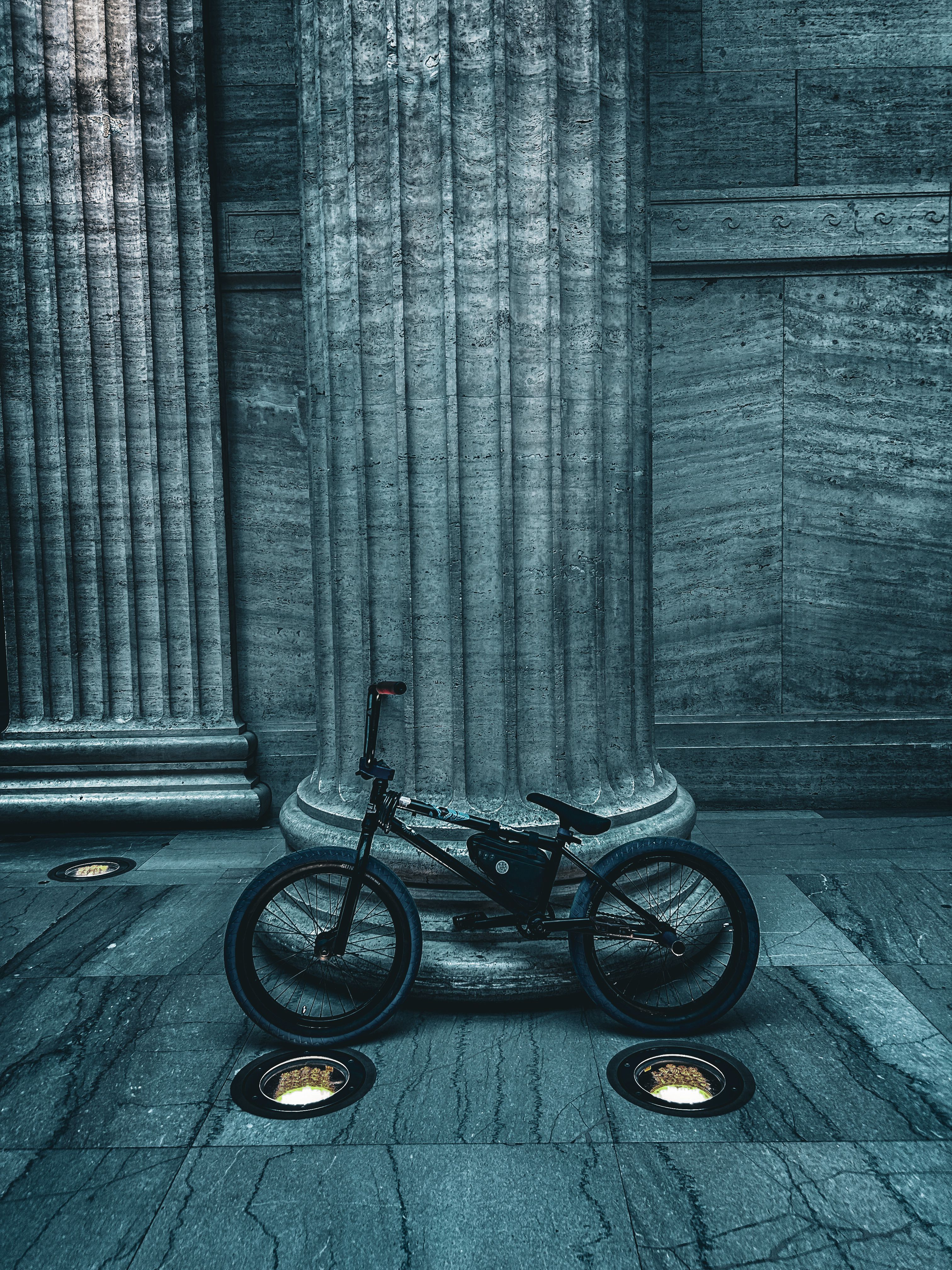 A bicycle parked in front of grand architectural columns in an urban setting.