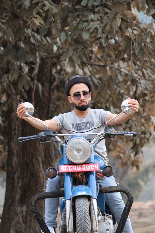 Free Man poses confidently on a vintage blue motorcycle in an outdoor setting. Stock Photo