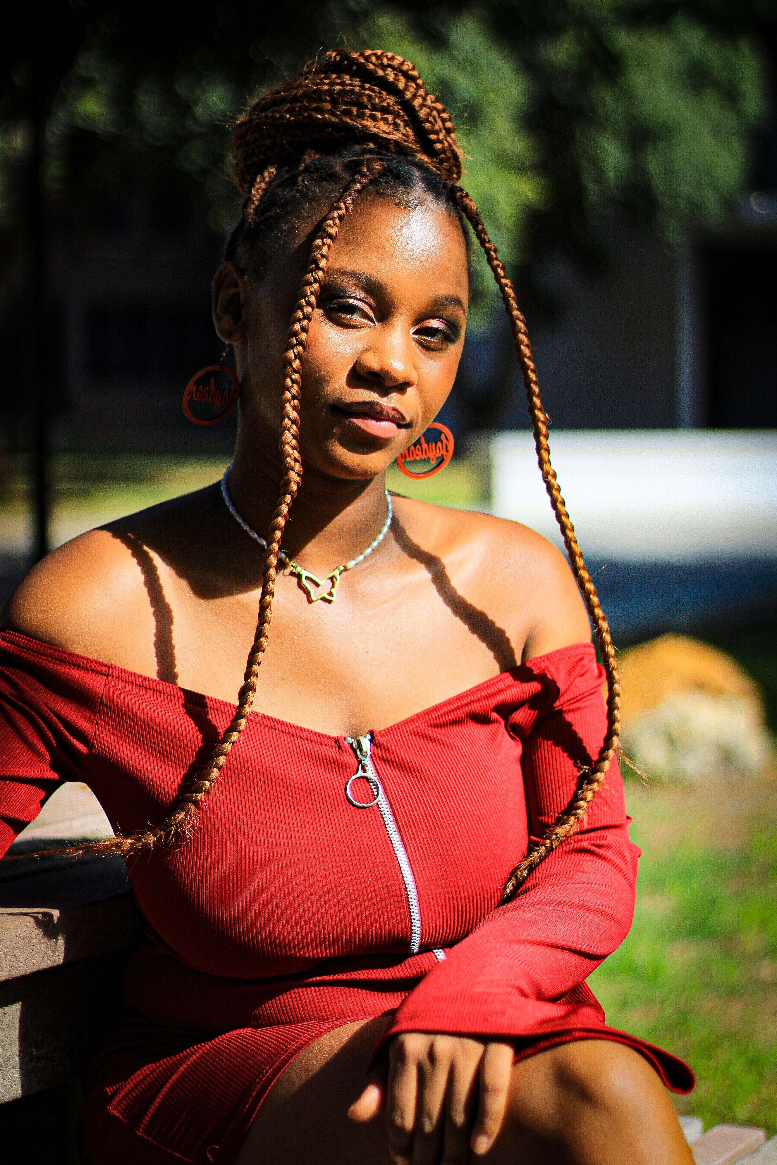 A woman with braided hair and stylish earrings poses in a red dress outdoors.