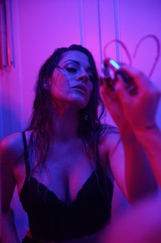 Moody portrait of a woman in lingerie under neon lighting, creating an artistic and edgy atmosphere.