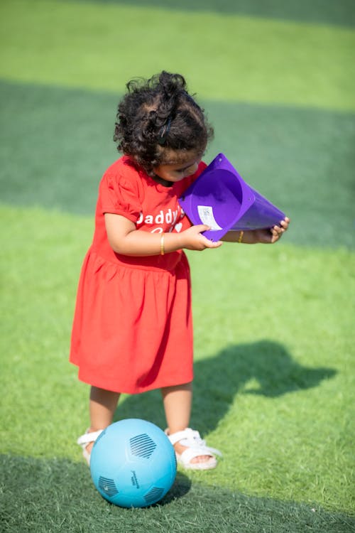 Little Girl Playing with Purple Cone and Blue Ball on Grass