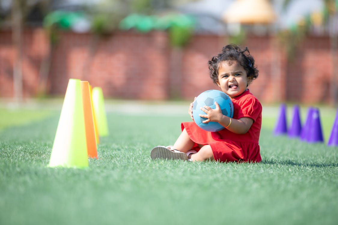 Little Girl Sitting with Blue Ball in Hands on Grass