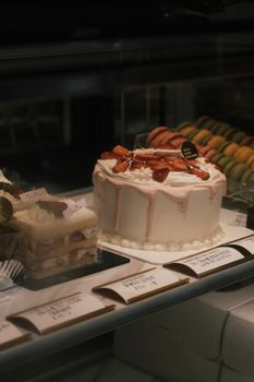 Close-up of a strawberry cake with macarons in a bakery display, perfect for food lovers.